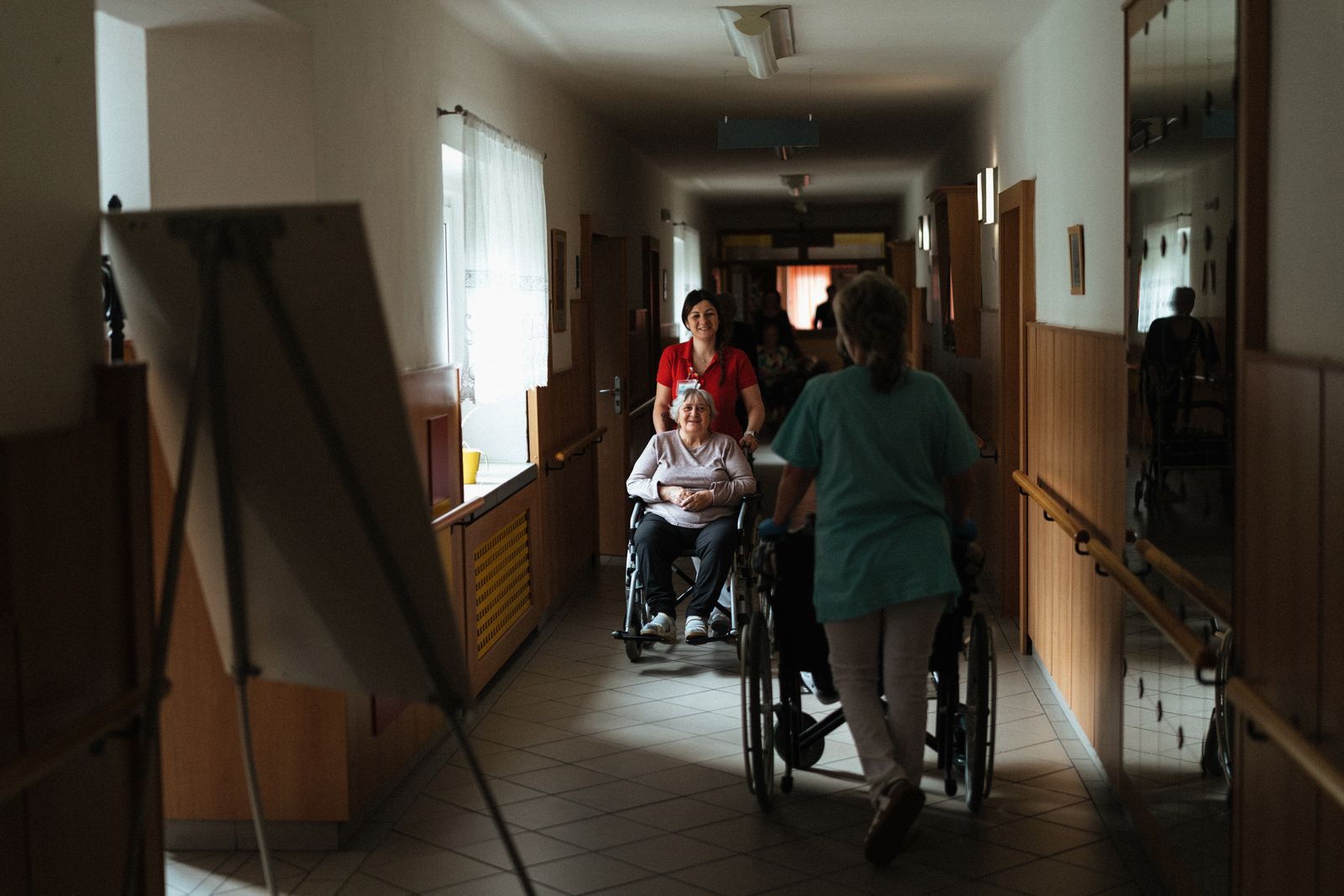Caregivers wheeling residents down a nursing home hallway