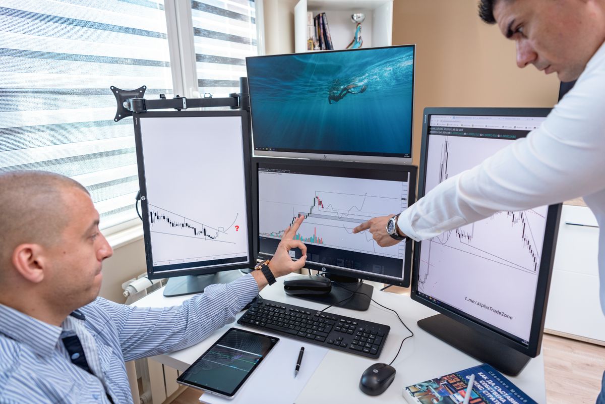 Analyst pointing at charts across multiple monitors